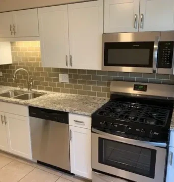 Modern kitchen with white cabinets, granite countertops, stainless steel appliances including a dishwasher, microwave, and gas stove. If you need updates or repairs, an Elmhurst handyman can help keep your space looking its best.