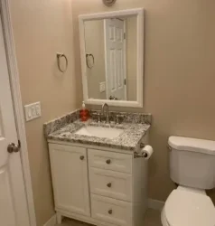 A small bathroom with a white vanity, granite countertop, mirror above the sink, a soap dispenser, and a white toilet next to the vanity—expertly refreshed by Brightwise Handyman. Beige walls and white doors complete the look.