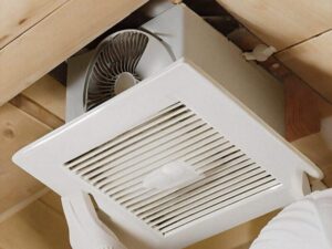 A person wearing a white glove performs a bathroom exhaust fan installation with a white vent cover in a wooden ceiling, demonstrating the electrical services offered by BrightWise Handyman.