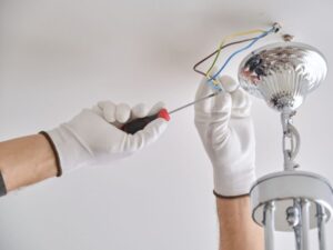 A person wearing white gloves uses a screwdriver to perform a light fixture installation, demonstrating the electrical services offered by BrightWise Handyman.