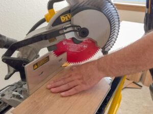 A carpenter's hand holds a wooden plank on a table saw while preparing to cut it with a circular saw in a well-lit indoor workshop, demonstrating the carpentry services offered by BrightWise Handyman.